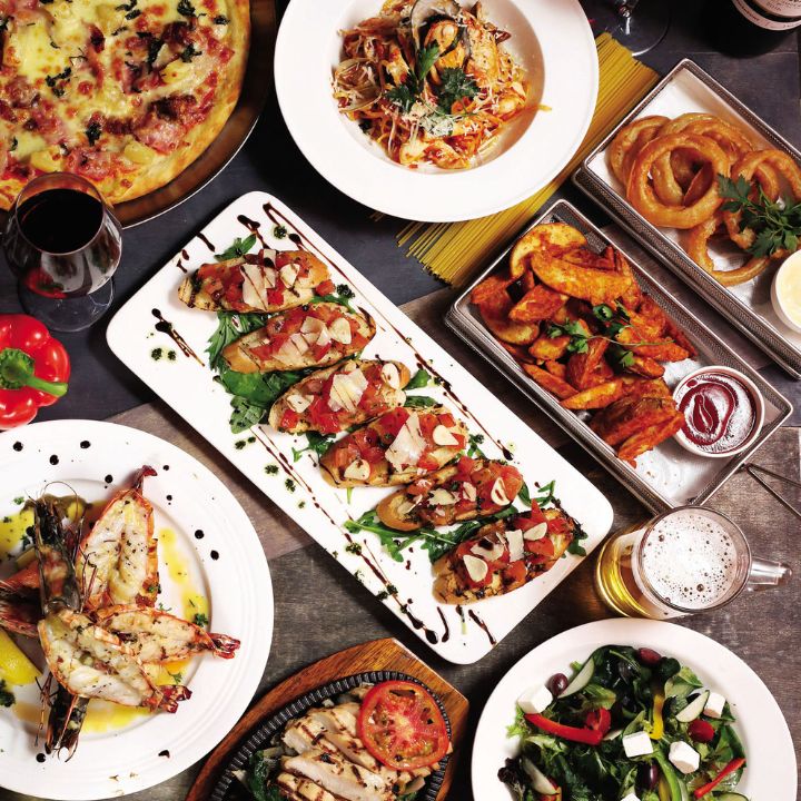 Assortment of pasta, pizza, grilled seafood, salad and side dishes, presented on white china with wine and beer glasses.