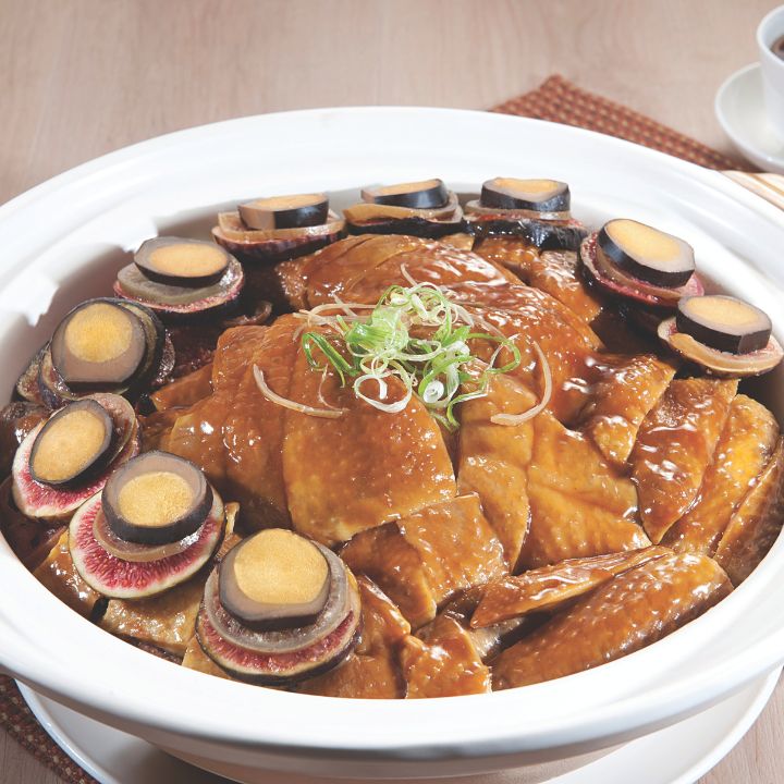 Chicken pieces in white ceramic pot with sliced figs and preserved lemon served with tea on woven red placemat.